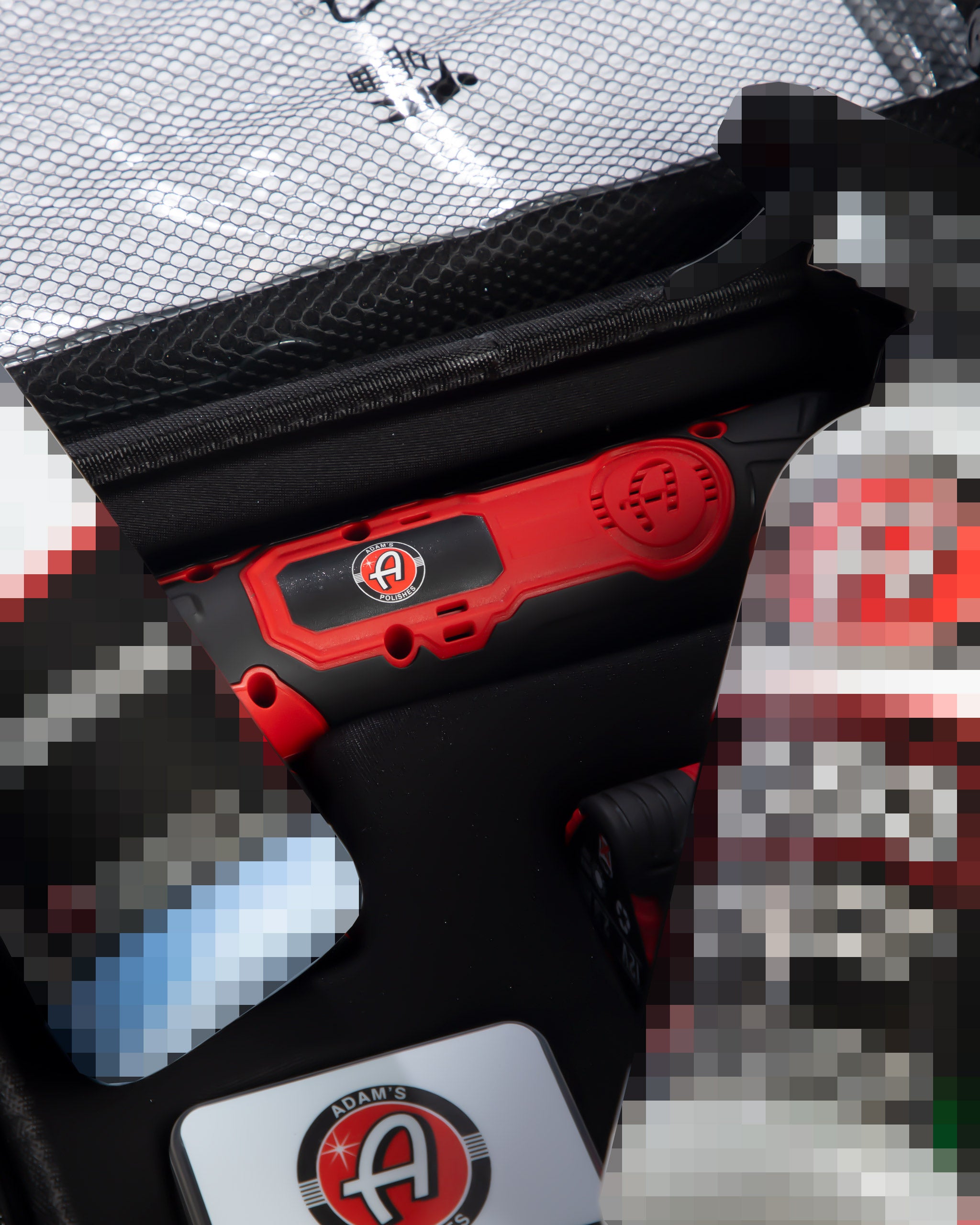 Alt text: Close-up view of Adam's SK Pro Micro Polisher 2.0 in red, partially visible with its distinctive logo on the handle, peeking out from a black mesh carrying bag, hinting at additional accessories, set against a