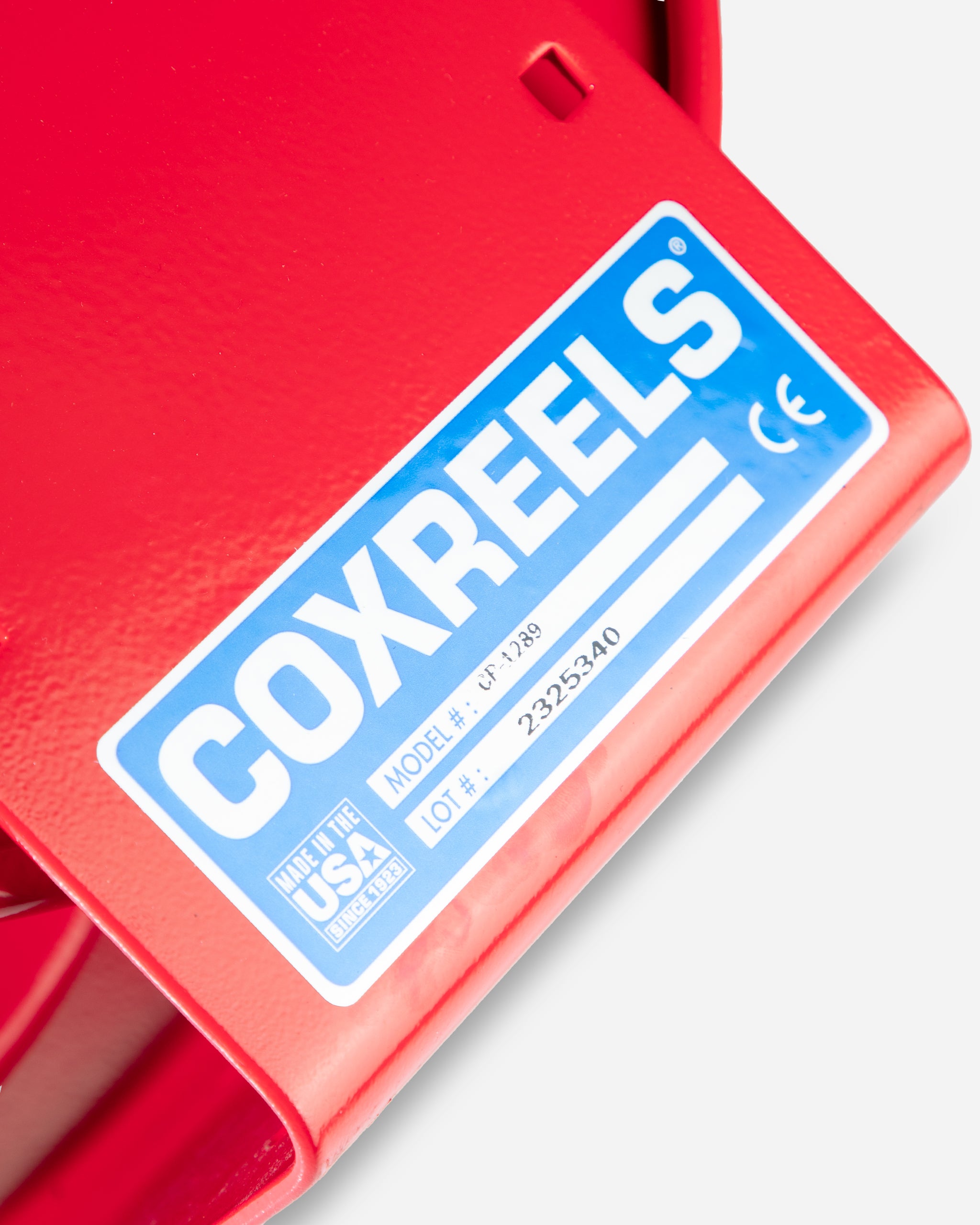 Close-up of a Coxreels brand hose reel model label in blue and white, mounted on a red surface, indicating "Made in the USA" and featuring model and lot numbers.
