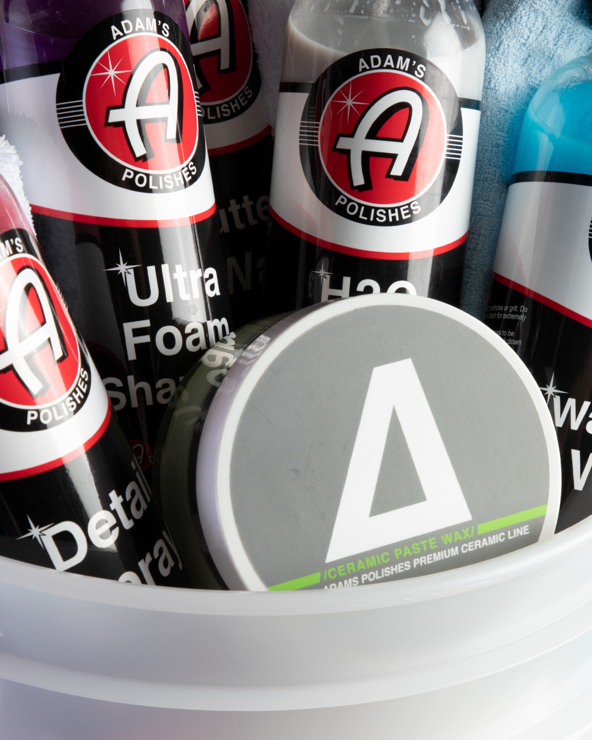 Alt text: Close-up view of Adam’s Mystery Bucket filled with various car care products including Ultra Foam Shampoo, H2O Guard & Gloss, and Ceramic Paste Wax, all branded with the Adam's Polishes logo.