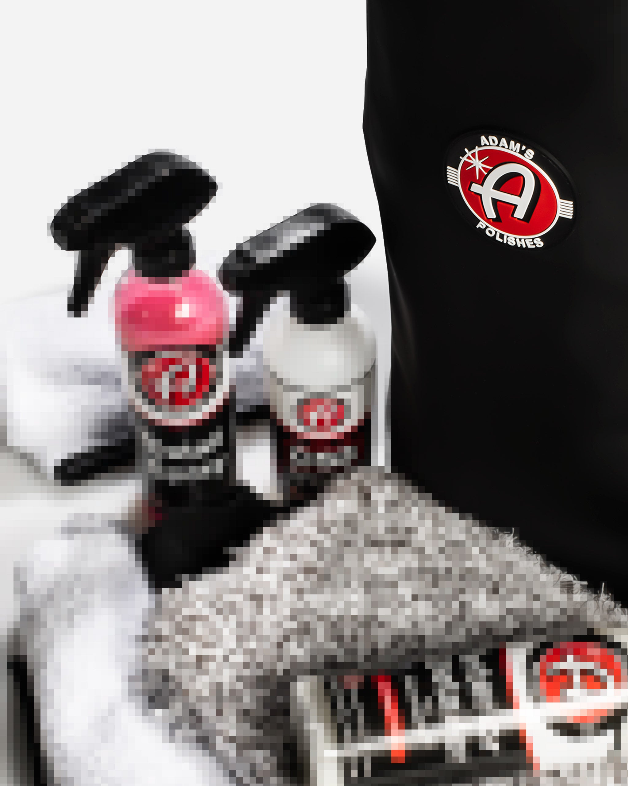 Alt text: Adam's Polishes $49.99 Mystery Drawstring Bag featuring an assortment of car care products including microfiber towels, spray bottles with pink and white solutions, and a black drawstring bag with Adam's Polishes logo on the front